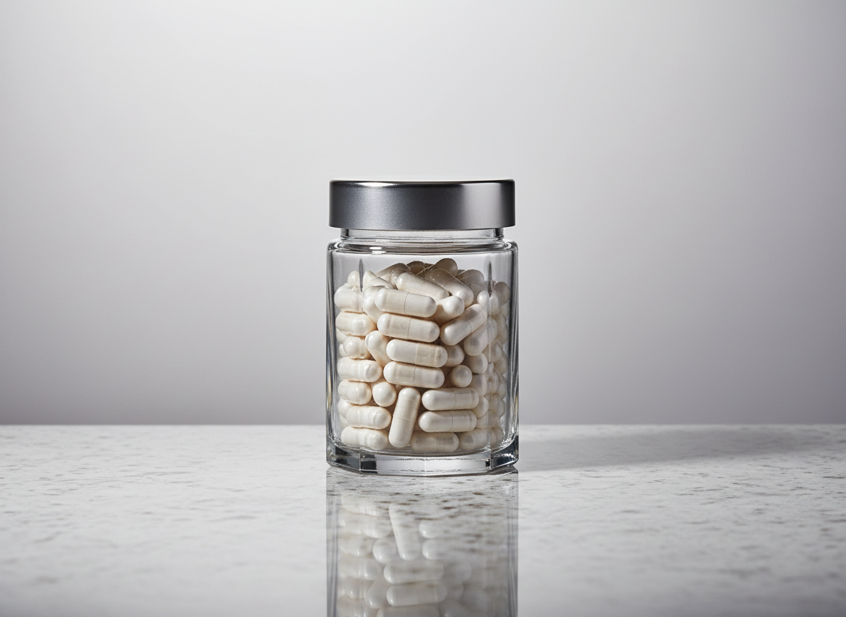 An elegant, crystal-clear glass supplement jar with an airtight brushed metal lid, filled with uniformly shaped white capsules. The jar is set on a smooth, light gray stone surface with crisp, linear shadows and immaculate reflections. The background showcases subtle vertical gradient tones in off-white and dove gray, emphasizing a structured, corporate environment. Cool, diffused studio lighting softly illuminates the jar, producing gentle highlights along its contours and adding sophisticated clarity. The mood is calm, professional, and trustworthy. Captured from a slightly elevated, centered perspective with a clean, minimalist composition and shallow depth of field, the image spotlights uncompromising purity and premium quality.